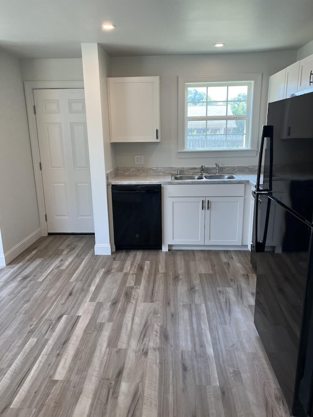 kitchen with white cabinets, light countertops, a sink, and black appliances
