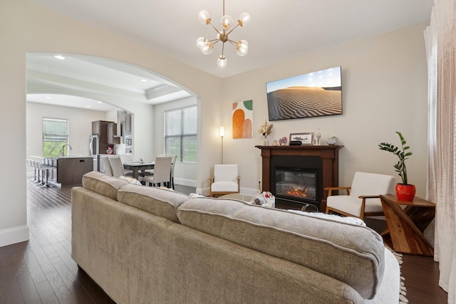 living room with a wealth of natural light, baseboards, arched walkways, and dark wood-style flooring