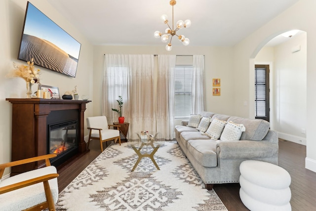 living room featuring arched walkways, dark wood-style flooring, baseboards, an inviting chandelier, and a glass covered fireplace