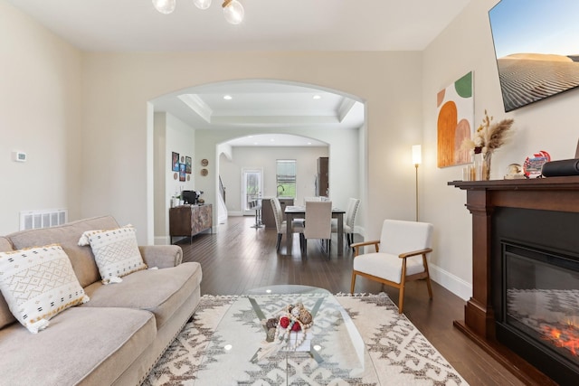 living area featuring a glass covered fireplace, arched walkways, dark wood finished floors, baseboards, and visible vents