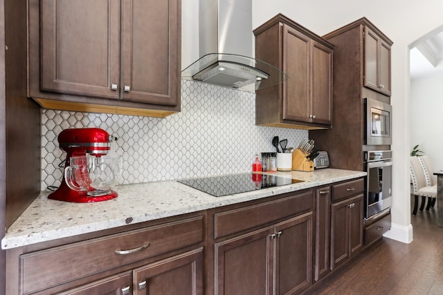 kitchen featuring stainless steel appliances, dark brown cabinets, wall chimney exhaust hood, decorative backsplash, and dark wood-style flooring
