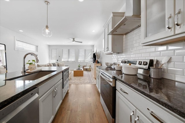 2123A 14th Ave N, Nashville, TN 37208 - kitchen featuring dark stone counters, a sink, light wood-type flooring, stainless steel appliances, and wall chimney exhaust hood