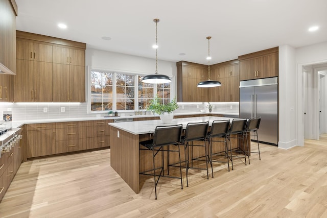 kitchen with light wood finished floors, a center island, tasteful backsplash, built in fridge, and a breakfast bar