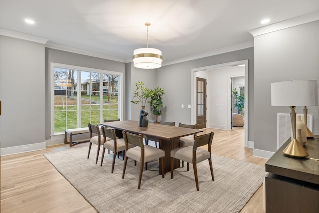 dining space featuring baseboards, light wood-style flooring, visible vents, and crown molding