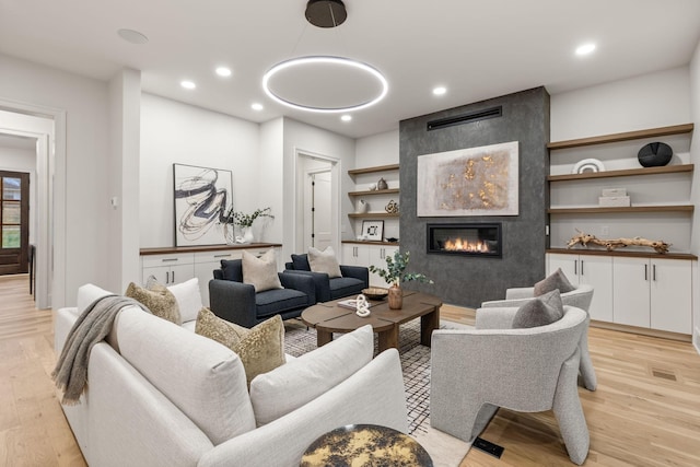 living area with recessed lighting, light wood finished floors, and a large fireplace