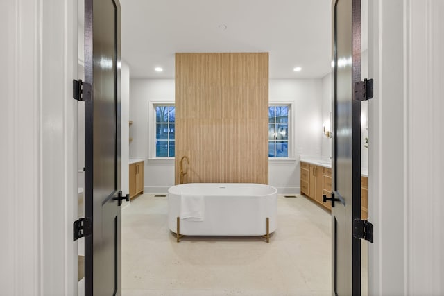 bathroom featuring vanity, baseboards, a soaking tub, and recessed lighting
