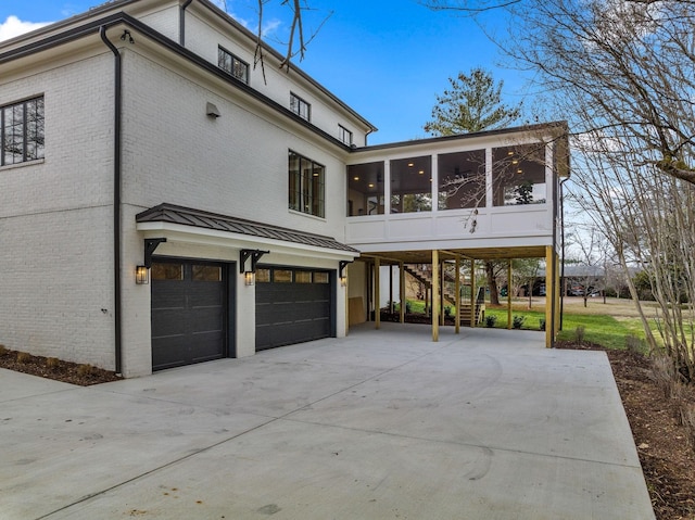 rear view of house with an attached garage, driveway, a sunroom, and brick siding