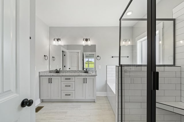 full bath with a bath, baseboards, a sink, and double vanity