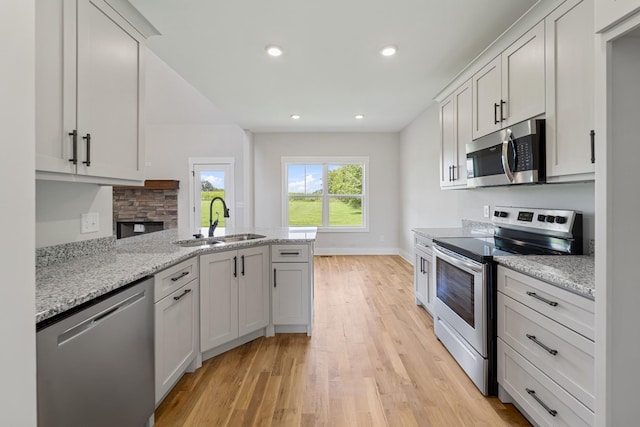kitchen with light wood finished floors, a peninsula, a sink, recessed lighting, and appliances with stainless steel finishes