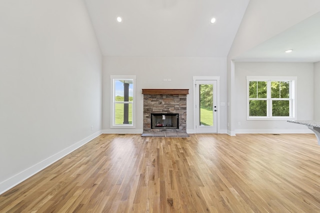 unfurnished living room featuring high vaulted ceiling, baseboards, a stone fireplace, and light wood-type flooring