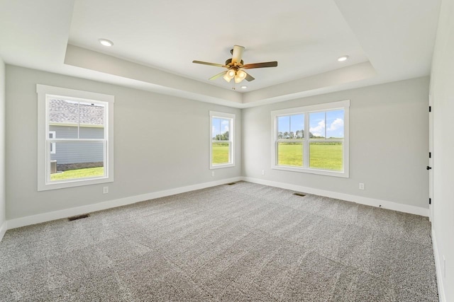 empty room with a ceiling fan, a tray ceiling, baseboards, carpet flooring, and visible vents