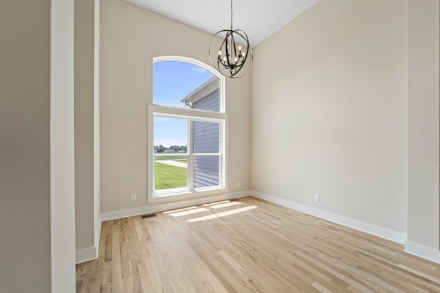 spare room featuring light wood-style flooring, baseboards, and an inviting chandelier