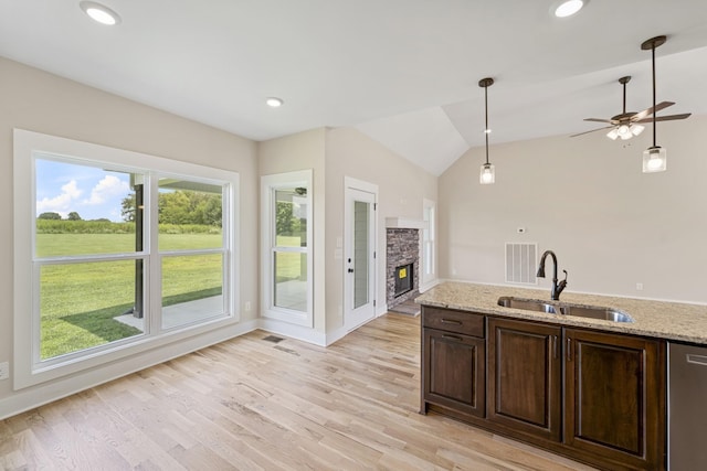 kitchen featuring stainless steel dishwasher, a sink, dark brown cabinetry, a fireplace, and hanging light fixtures
