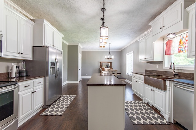 kitchen with a center island, a sink, a textured ceiling, dark countertops, and appliances with stainless steel finishes
