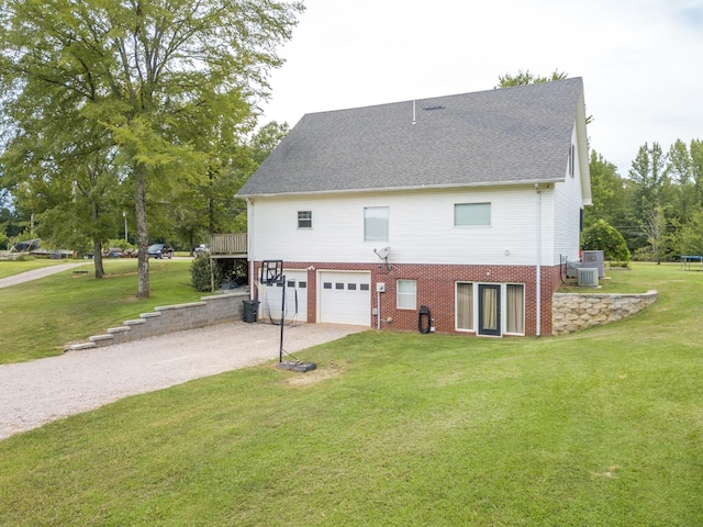 exterior space featuring central AC, brick siding, an attached garage, a yard, and gravel driveway