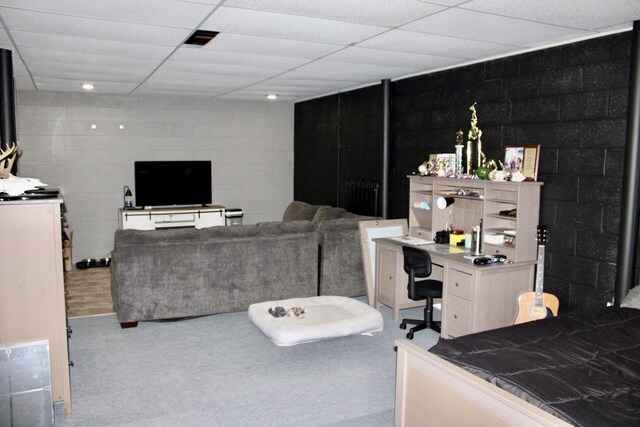 living room featuring concrete block wall, carpet flooring, and a drop ceiling