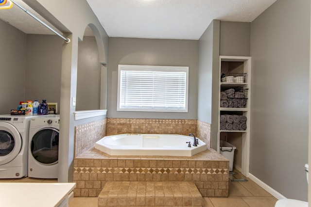 full bath featuring washing machine and clothes dryer, tile patterned floors, and a garden tub