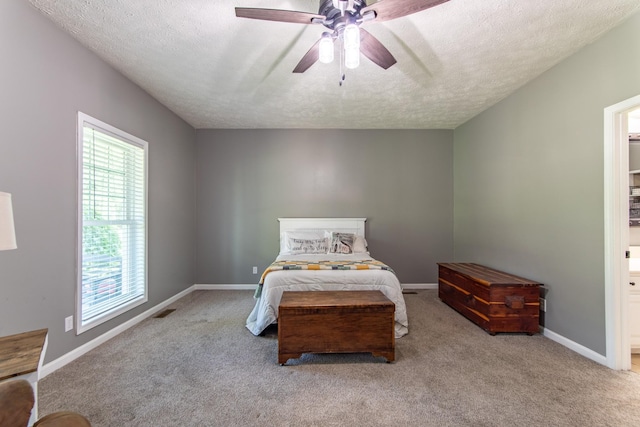 carpeted bedroom featuring visible vents, ensuite bath, baseboards, a textured ceiling, and ceiling fan