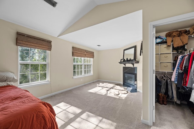 carpeted bedroom with vaulted ceiling, a walk in closet, a closet, baseboards, and a glass covered fireplace