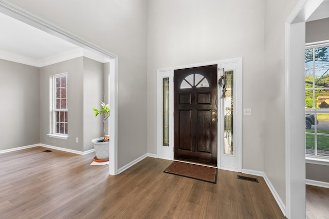 entrance foyer featuring visible vents, baseboards, wood finished floors, and ornamental molding