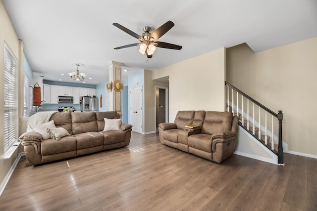 living room with hardwood / wood-style flooring, baseboards, stairway, and ceiling fan with notable chandelier