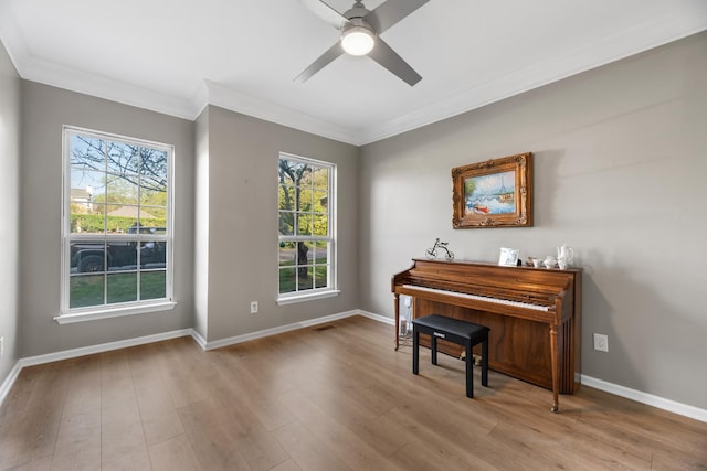 sitting room with wood finished floors, a wealth of natural light, crown molding, baseboards, and ceiling fan
