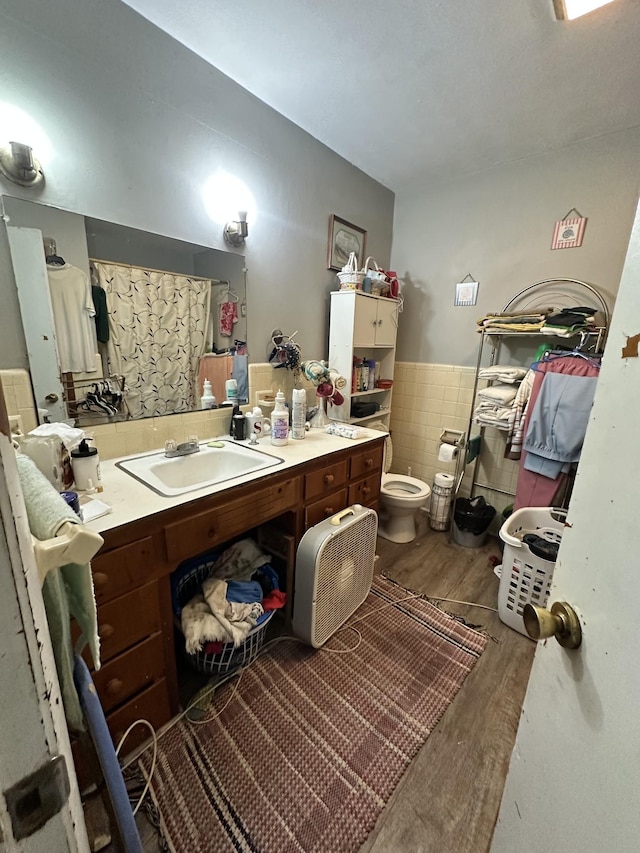 bathroom featuring wood finished floors, wainscoting, vanity, tile walls, and toilet
