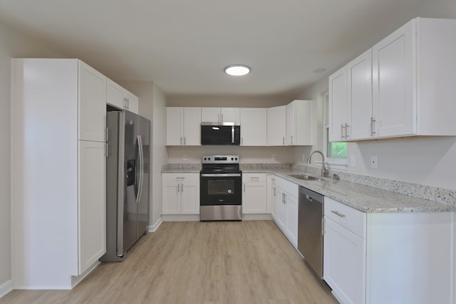 kitchen with white cabinetry, a sink, appliances with stainless steel finishes, light wood-style floors, and light stone countertops
