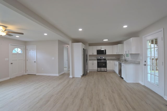 kitchen with appliances with stainless steel finishes, open floor plan, light wood-style floors, and baseboards