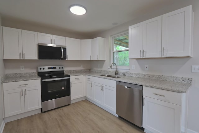 kitchen featuring appliances with stainless steel finishes, white cabinetry, light wood-type flooring, and a sink