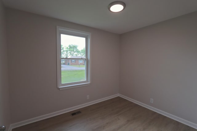 unfurnished room featuring baseboards, visible vents, and wood finished floors