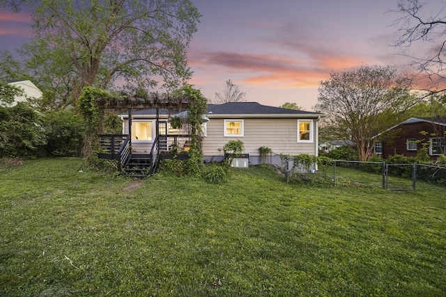 back of property at dusk with a wooden deck, a yard, fence, and a gate