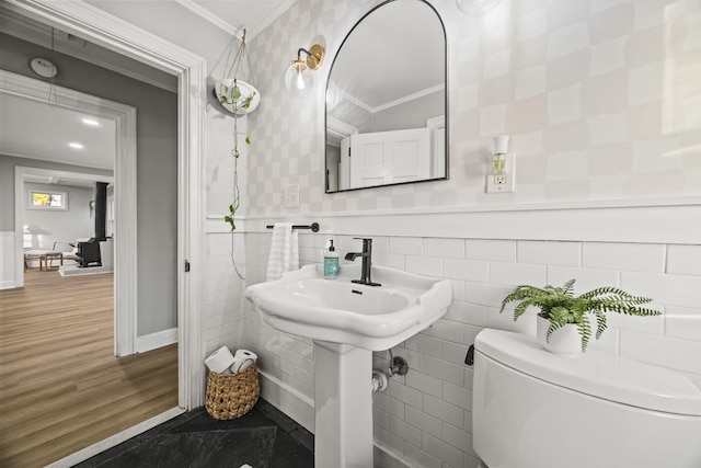 bathroom featuring a wainscoted wall, toilet, ornamental molding, tile walls, and baseboards