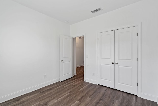 unfurnished bedroom with baseboards, visible vents, dark wood-style floors, and a closet