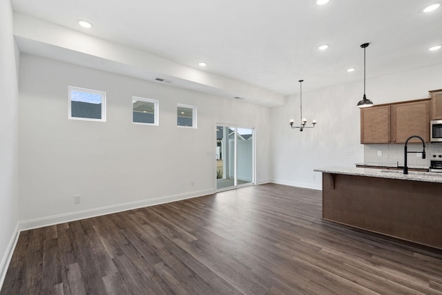 kitchen with dark wood finished floors, a sink, stainless steel microwave, baseboards, and hanging light fixtures
