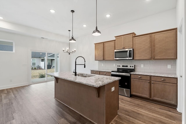 kitchen with stainless steel appliances, backsplash, a sink, dark wood-type flooring, and a center island with sink