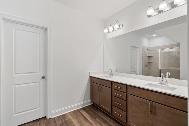 bathroom featuring wood finished floors, a sink, a shower stall, and double vanity