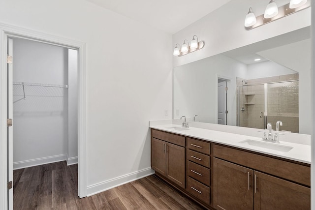 bathroom with wood finished floors, a sink, a shower stall, and a walk in closet