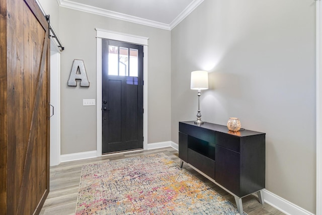 entrance foyer featuring baseboards, light wood-style floors, ornamental molding, and a barn door