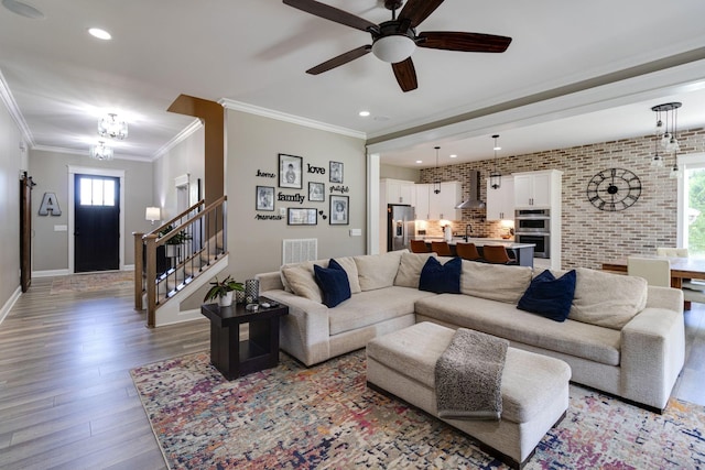 living room featuring visible vents, ceiling fan with notable chandelier, wood finished floors, stairway, and ornamental molding