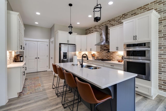 kitchen featuring wall chimney range hood, a sink, light countertops, backsplash, and appliances with stainless steel finishes