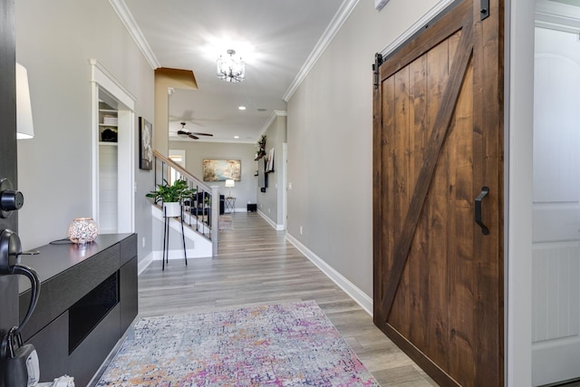 hall with crown molding, light wood-style floors, stairway, and a barn door