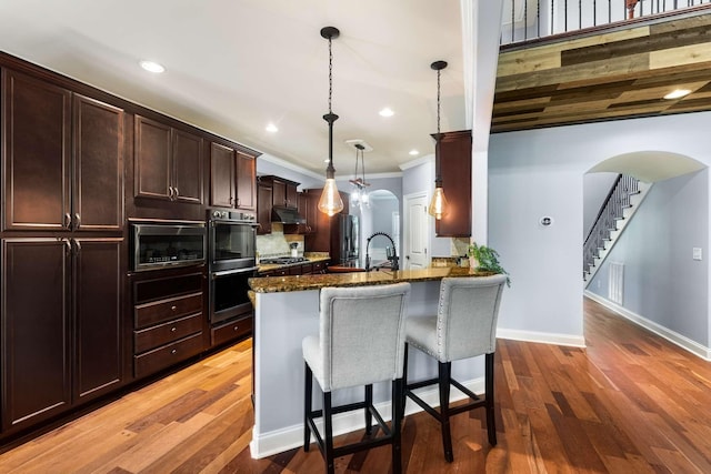 5000 Moretto Ct, Spring Hill, TN 37174 - kitchen featuring stainless steel appliances, arched walkways, dark stone countertops, a breakfast bar, and dark brown cabinetry