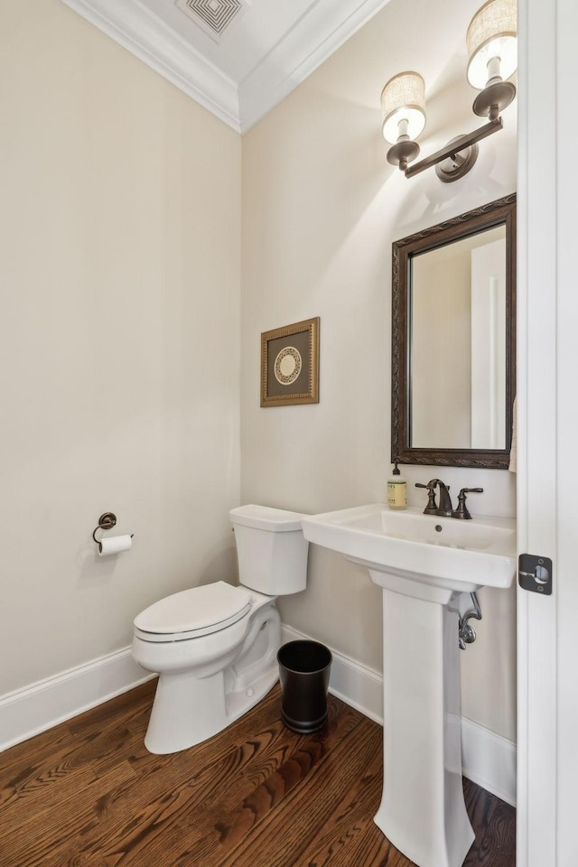 half bath featuring toilet, visible vents, baseboards, wood finished floors, and ornamental molding