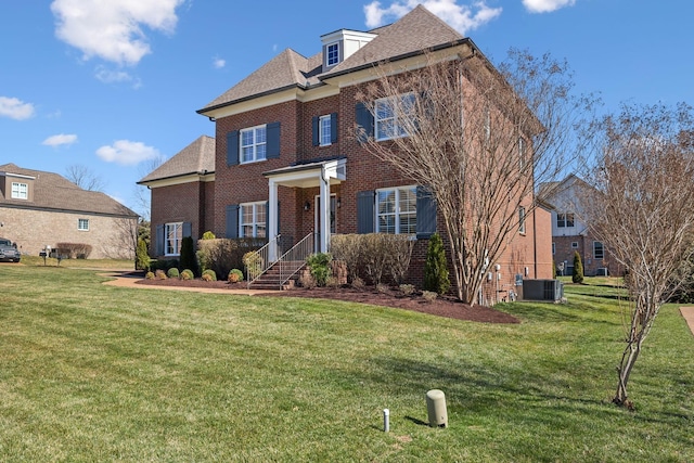 colonial inspired home with central AC unit, brick siding, a shingled roof, and a front yard