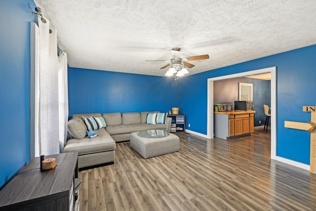 living room featuring ceiling fan, baseboards, wood finished floors, and a textured ceiling