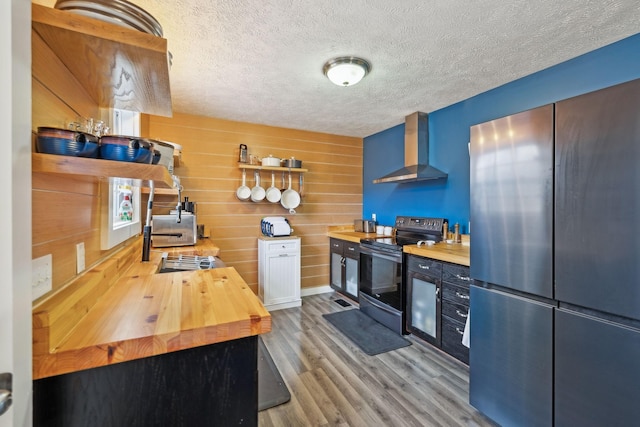 kitchen with wall chimney exhaust hood, stainless steel appliances, light wood finished floors, a textured ceiling, and wooden counters