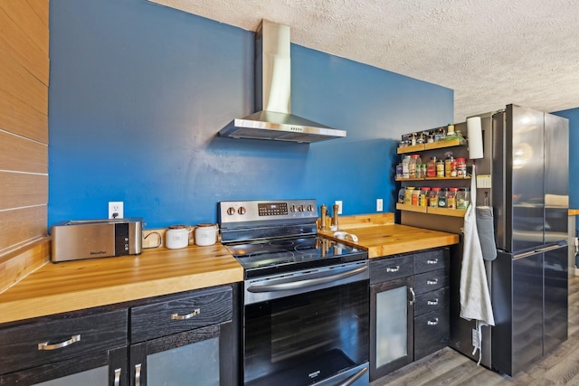 kitchen featuring wooden counters, wood finished floors, wall chimney exhaust hood, a textured ceiling, and appliances with stainless steel finishes
