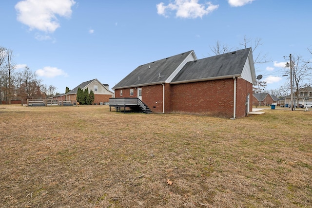 rear view of property featuring brick siding, a lawn, and a wooden deck