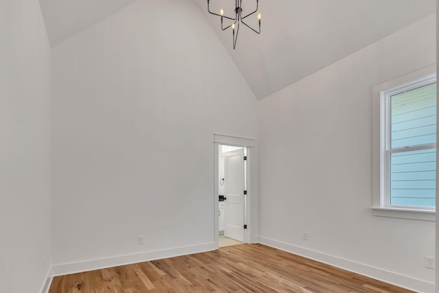 unfurnished room with light wood-style flooring, baseboards, an inviting chandelier, and high vaulted ceiling